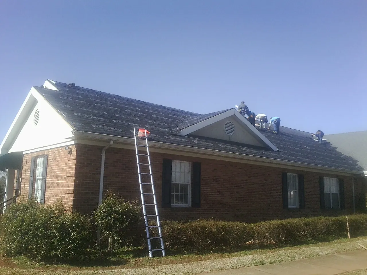 Crew tearing shingles off a brick ranch roof with a ladder set — Metal Roof Repair work by our crew in Rosemont