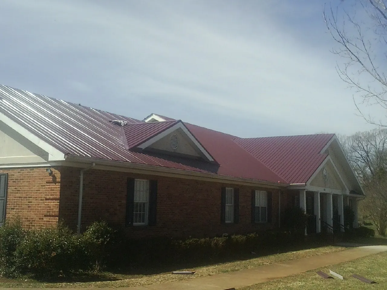 Red metal roof with gabled entries on a long brick building, from a Hail Damage Roof Repair job in Rosemont