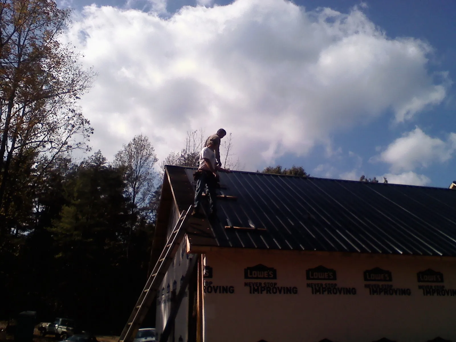 Roofer fastening dark metal panels high against a cloudy sky, from a Roof Inspection job in Rosemont