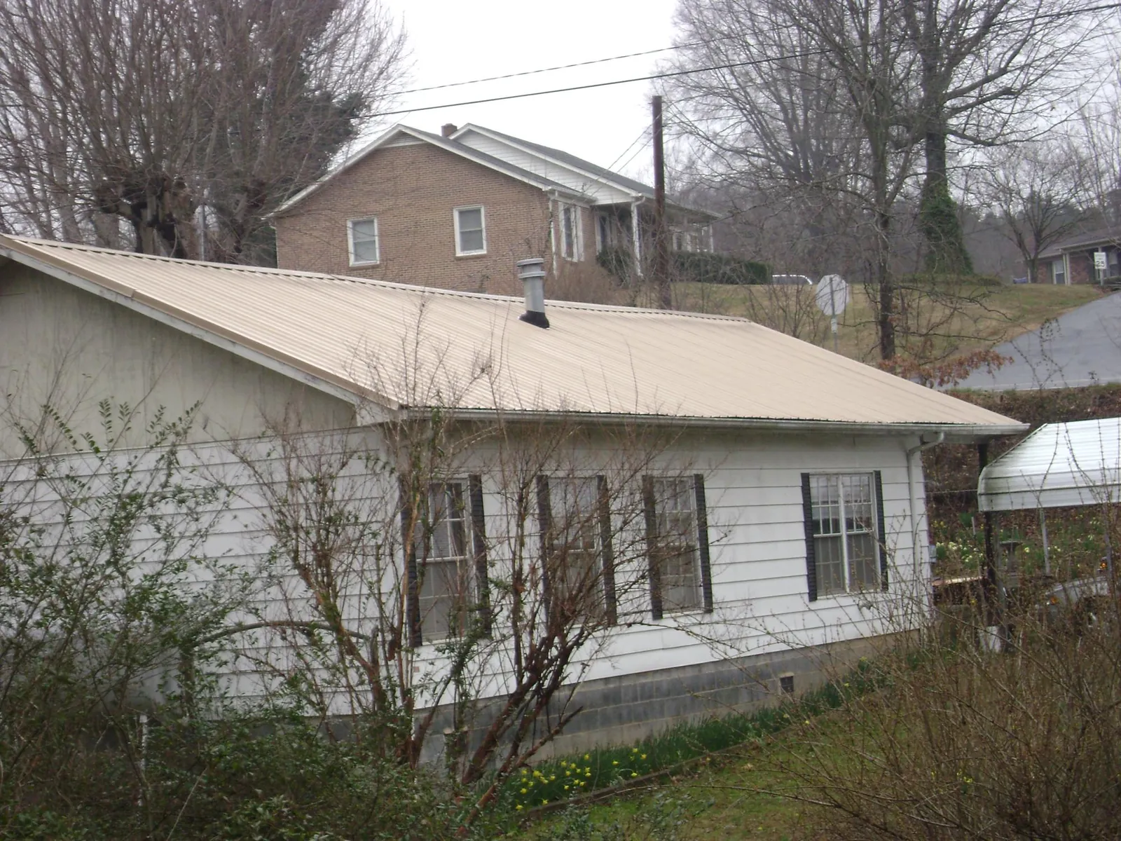 Tan metal roof on a white sided house set into a hillside — Commercial Roofing by Roofing Brothers in Rosemont